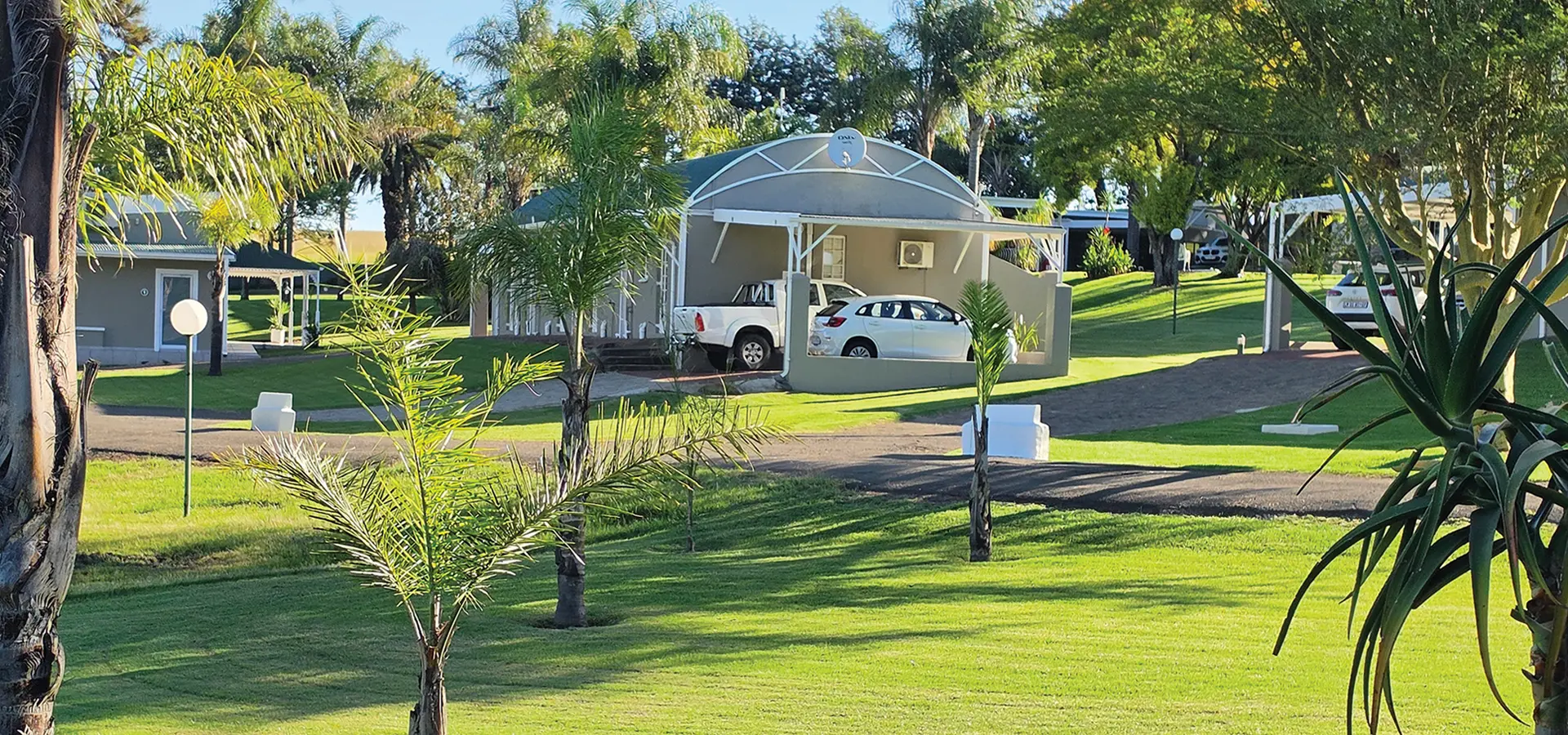 Lawns, palms and lodge buildings with covered parking at Newcastle Country Lodge